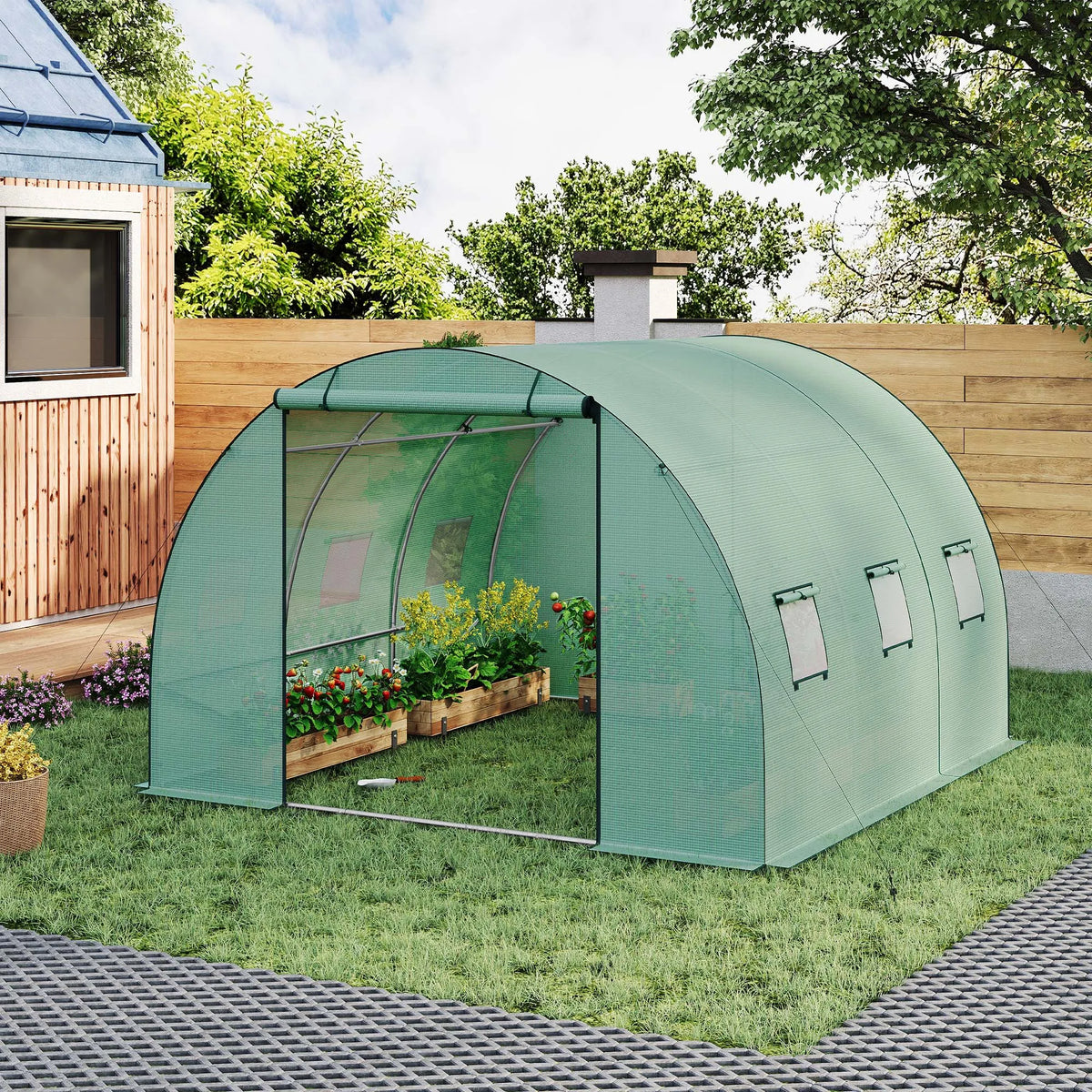 Groene tunnelkas in de tuin met open oproldeur, zijramen en bloeiende planten binnen