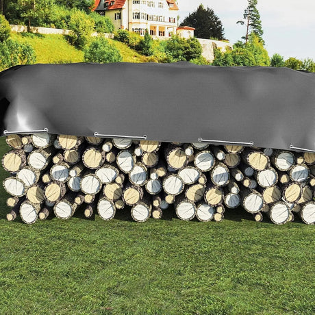 Grijs afdekzeil over een houtstapel in de tuin, met zichtbare zeilogen langs de rand