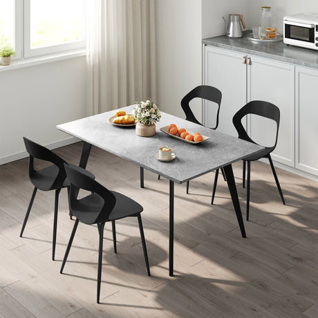 Vier zwarte eetkamerstoelen met open rugleuning rond een eettafel in een lichte keuken
